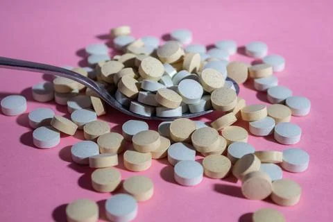Multicolored round medical pills scattered from a spoon on a pink background Stock Photos