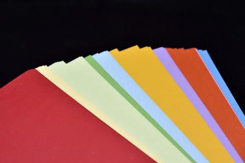 Multicolored sheets of paper on a black background. Colored office paper. A.. Stock Photos