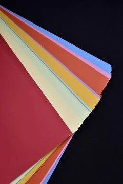 Multicolored sheets of paper on a black background. Colored office paper. A.. Stock Photos