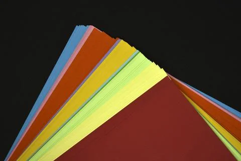 Multicolored sheets of paper on a black background. Colored office paper. A.. Stock Photos