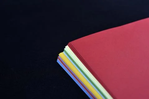 Multicolored sheets of paper on a black background. Colored office paper. A.. Stock Photos