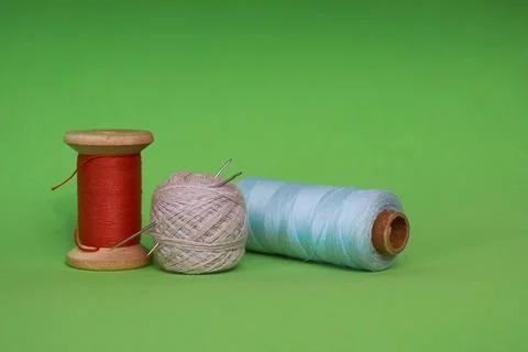 Multicolored spools of thread and a sewing needle on a green background Stock Photos