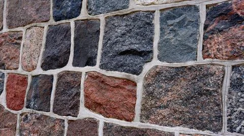 A multicolored stone wall with irregular rectangular blocks and white grout. Stock Photos