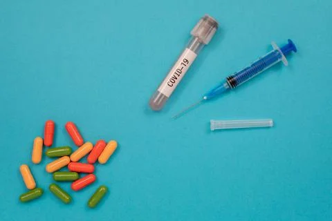 Multicolored tablets are scattered on the table, a syringe, a needle, a test Stock Photos