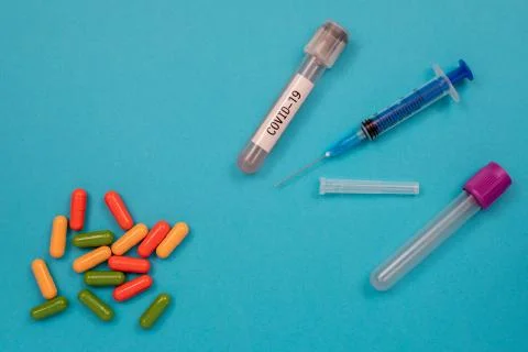 Multicolored tablets are scattered on the table, a syringe, a needle, a test Stock Photos