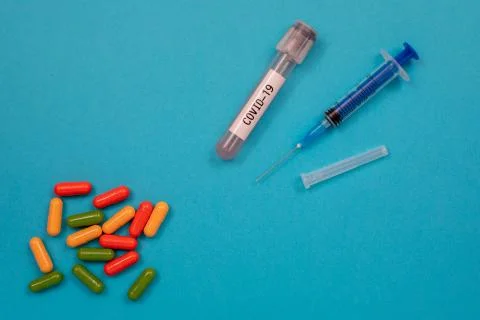 Multicolored tablets are scattered on the table, a syringe, a needle, a test Stock Photos
