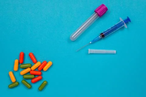Multicolored tablets are scattered on the table, a syringe, a needle, a test Stock Photos