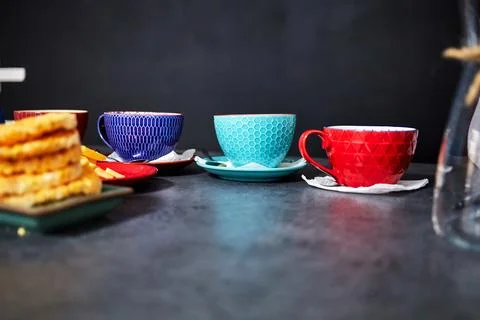 Multicolored tea cups on the table against a black wall background Stock Photos