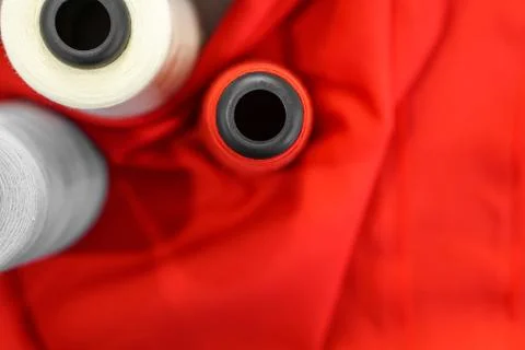 A multicolored thread spool placed on a red fine fabric. Stock Photos