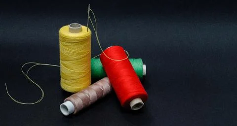 Multicolored threads with scissors and a button on a black background Stock Photos