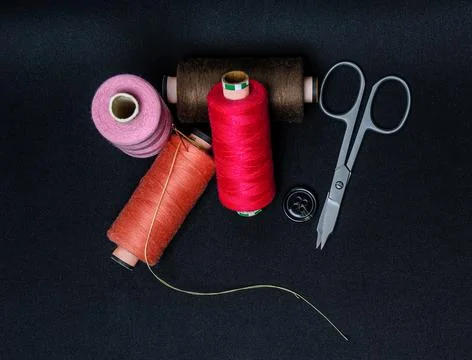 Multicolored threads with scissors and a button on a black background 写真素材