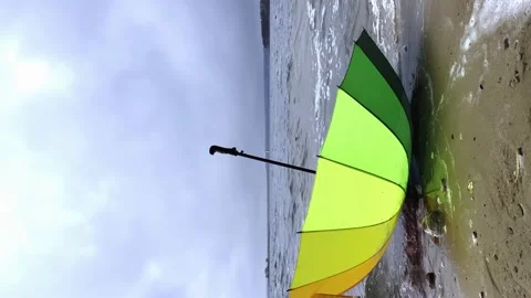 A multicolored umbrella washed ashore by waves, cloudy windy weather Stock Footage 238551064