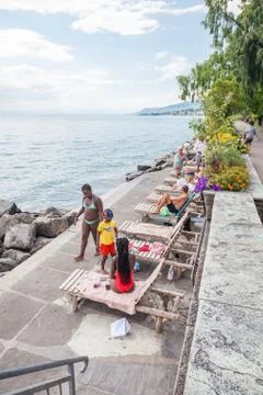 Multicultural community sunbathing on beach along Geneva lakeside and Montreu Stock Photos
