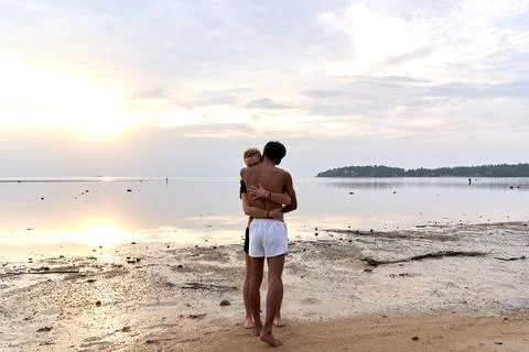 Multicultural couple embracing while standing next to the sea during sunset Stock Photos