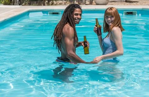 Multicultural couple inside an outdoor pool with a beer in hand Stock Photos