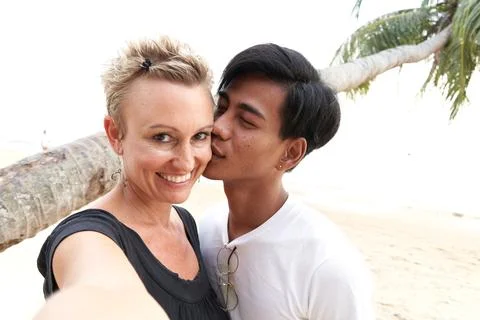 Multicultural couple kissing while taking a selfie on the beach during sunset Foto stock