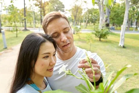 Multicultural couple looking and picking white flowers in an urban park Stock Photos