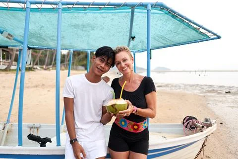 Multicultural couple looking at camera while drinking coconut on the beach Stock Photos