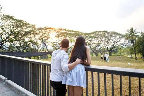 Multicultural couple looking the landscape of a park during sunset Stock Photos