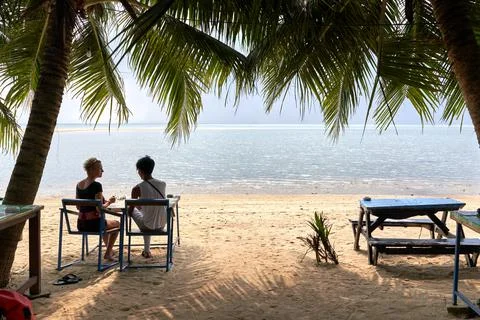 Multicultural couple sitting on a beach looking to the horizon while talking Stock Photos