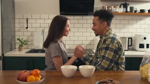 Multicultural couple sitting at kitchen table holding hands. Video stock 305651704