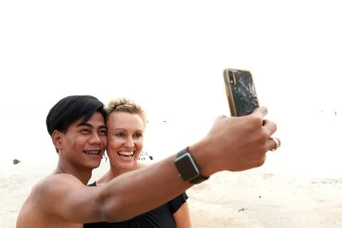 Multicultural couple taking a selfie with a mobile on the beach Stock Photos