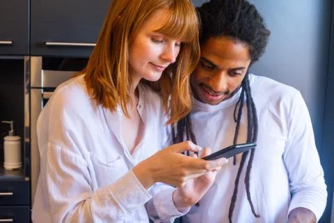 Multicultural couple watching the mobile in the kitchen Stock Photos