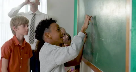 Multicultural elementary pupil group writes math answer on green chalkboard Stock Footage 337465573