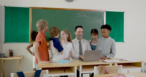 Multicultural elementary student group gathers around male teacher using laptop Stock Footage 335459819