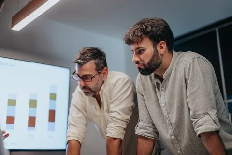 Multicultural executives discuss architectural blueprints and graph charts in a Stock Photos