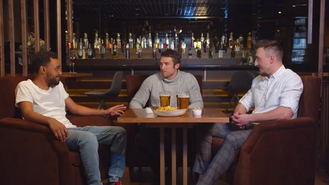 Multicultural friends sit at the bar, drink beer and chat Stock Footage 123680439