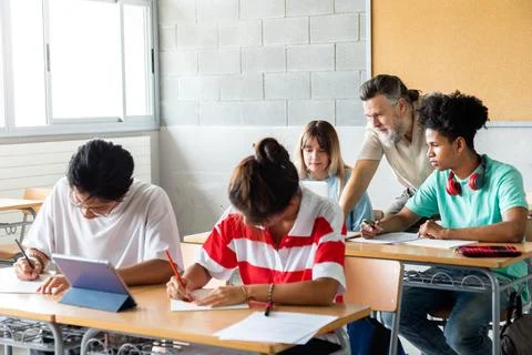 Multicultural group of high school students do homework in class while mature Stock Photos
