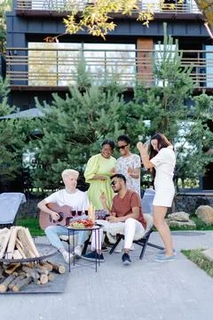 Multicultural group of people, man playing guitar and friends dancing, sing.. Stock Photos