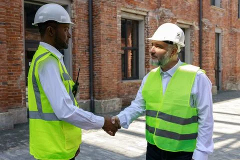 Multicultural men in helmets and reflective vests greeting each other with hand Stock Photos