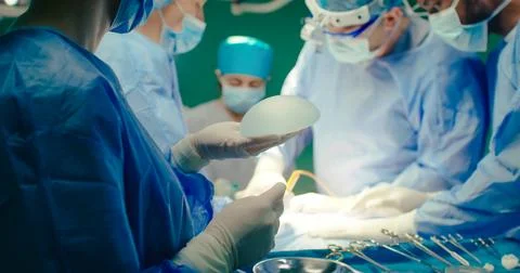 Multicultural team of professional plastic surgeons performs plastic surgery in Stock Photos