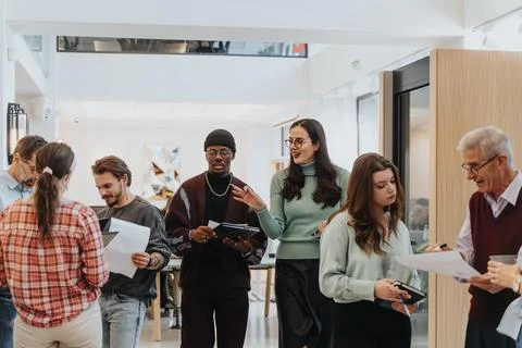 A multicultural team of professionals discusses work documents in a cozy, light Stock Photos