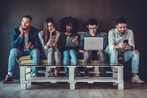 Multicultural young people using laptops and smartphones sitting in row Foto stock