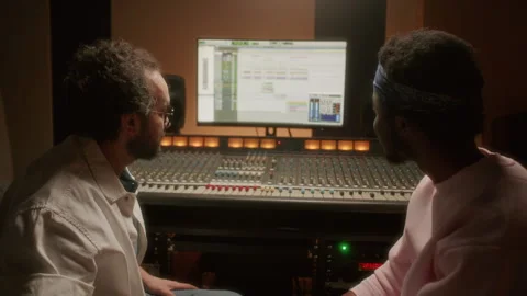 Multiethnic Audio Engineer and Musician Talking and Using Studio Mixing Desk Stock Footage 334365634