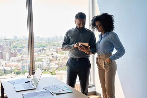 Multiethnic colleagues standing using tablet discussing project in office. Stock Photos