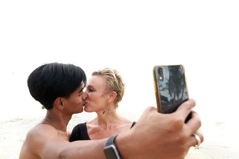 Multiethnic couple kissing while taking a selfie on a beach Stock Photos