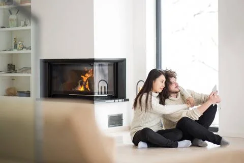 Multiethnic couple using tablet computer in front of fireplace beautiful y... Stock Photos