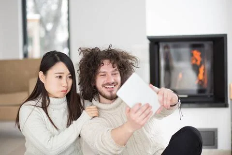 Multiethnic couple using tablet computer in front of fireplace beautiful y... Stock Photos