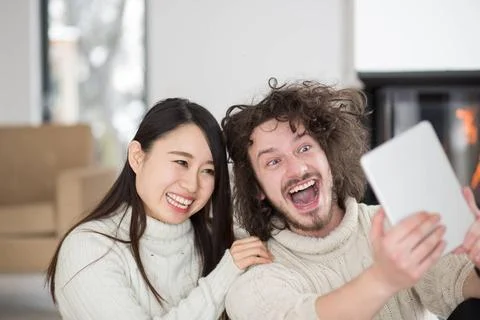 Multiethnic couple using tablet computer in front of fireplace beautiful y... Stock Photos