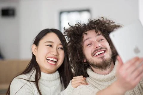 Multiethnic couple using tablet computer in front of fireplace beautiful y... Stock Photos