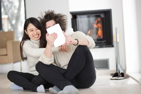 Multiethnic couple using tablet computer in front of fireplace beautiful y... Stock Photos