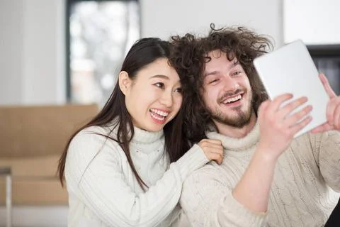 Multiethnic couple using tablet computer in front of fireplace beautiful y... Stock Photos