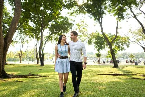 Multiethnic couple walking while embracing looking each other in a park Stock Photos