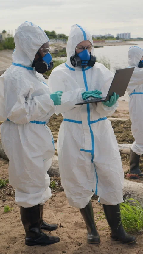 Multiethnic Ecologists in Hazmat Suits Using Laptop on Polluted Beach 動画素材 344717112