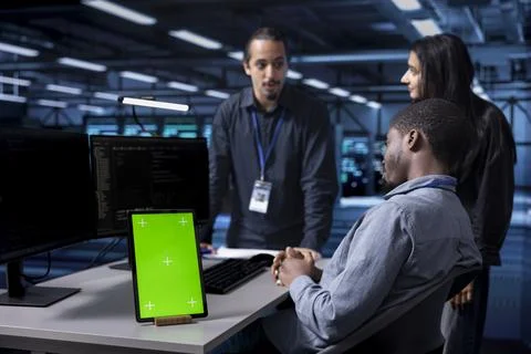 Multiethnic engineering team works on green screen tablet in data center Stock Photos