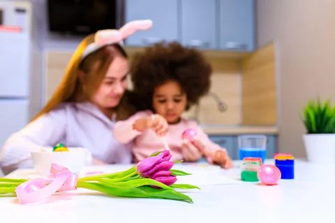 Multiethnic family preparing to easter event at kitchen painting eggs Stock Photos